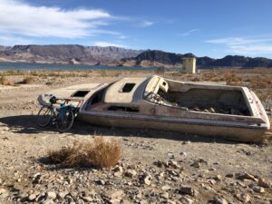 Bike, leaning against wrecked speedboats, with reservoir in the background.