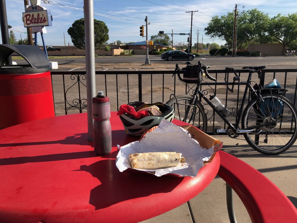 Burrito on red picnic table with bicycle and street in background.