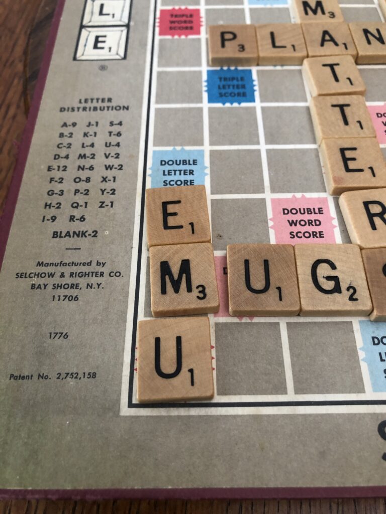 A board for the game Scrabble with the words “emu” and “mug” spelled out with game tiles.