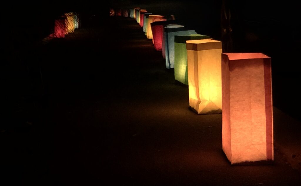 Row of multi-colored paper bags lit from within by candles.