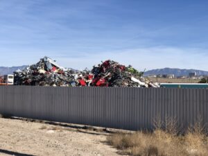 Fence in the foreground with a junkyard pile rising behind it and mountains in the distance.