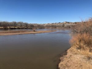 River in the foreground, with bluffs in the distance. Plants still have the browns of winter.